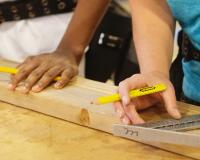 a carpenter apprentice measuring and cutting a board