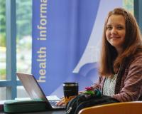 Pre-professional health professions student with a laptop smiles in a sunny lobby
