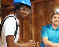 two construction technology students, one wearing PPE, pose and smile in the frame of a wall they're building