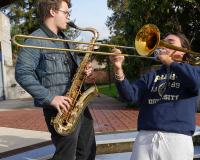 three music students play an electric guitar, a saxophone, and a trumpet outside the LCC music building