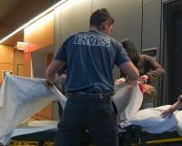 two EMT/Paramedicine students practice moving a dummy onto a gurney in the Health Professions building