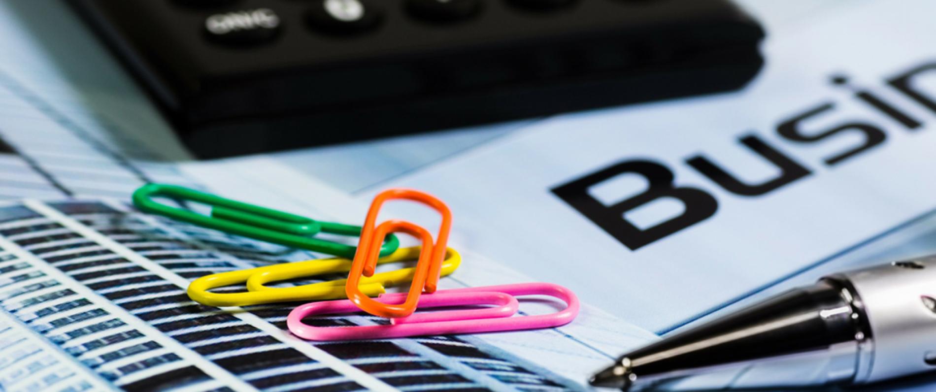 close up of a stack of papers with colorful paperclips, a pen, and a calculator on top