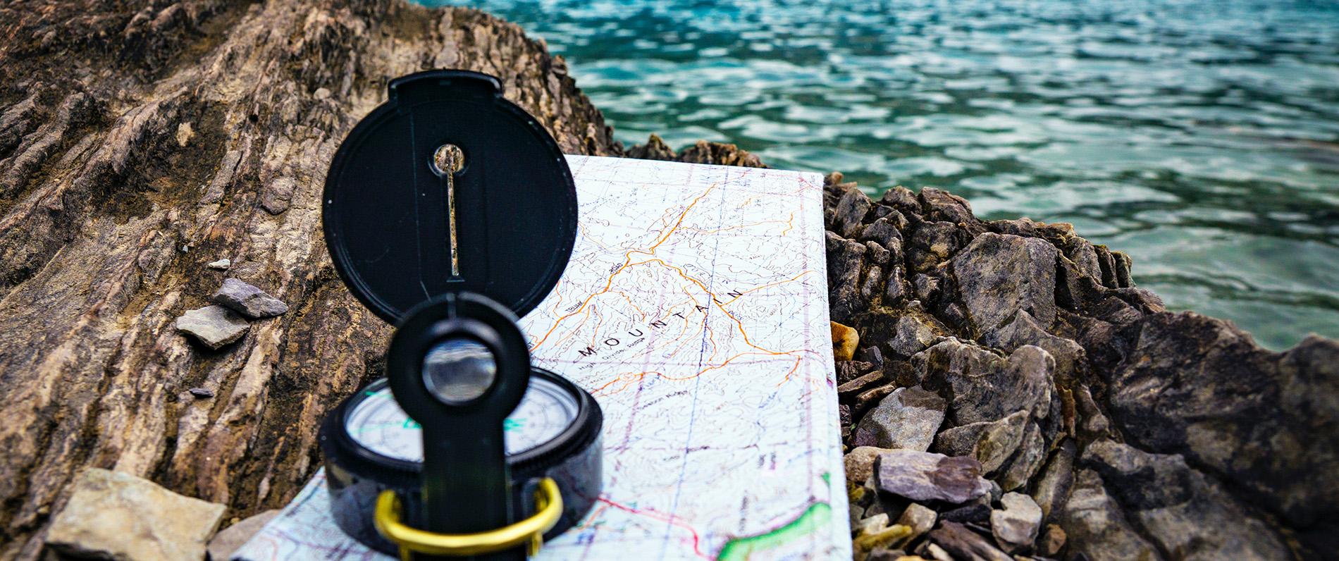 a compass sitting on a map on some rocks by a lake