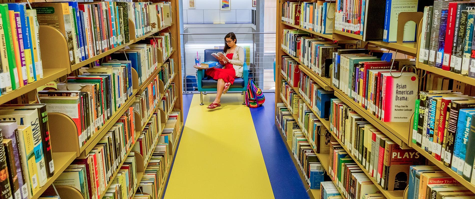 woman reading a book in between bookshelves