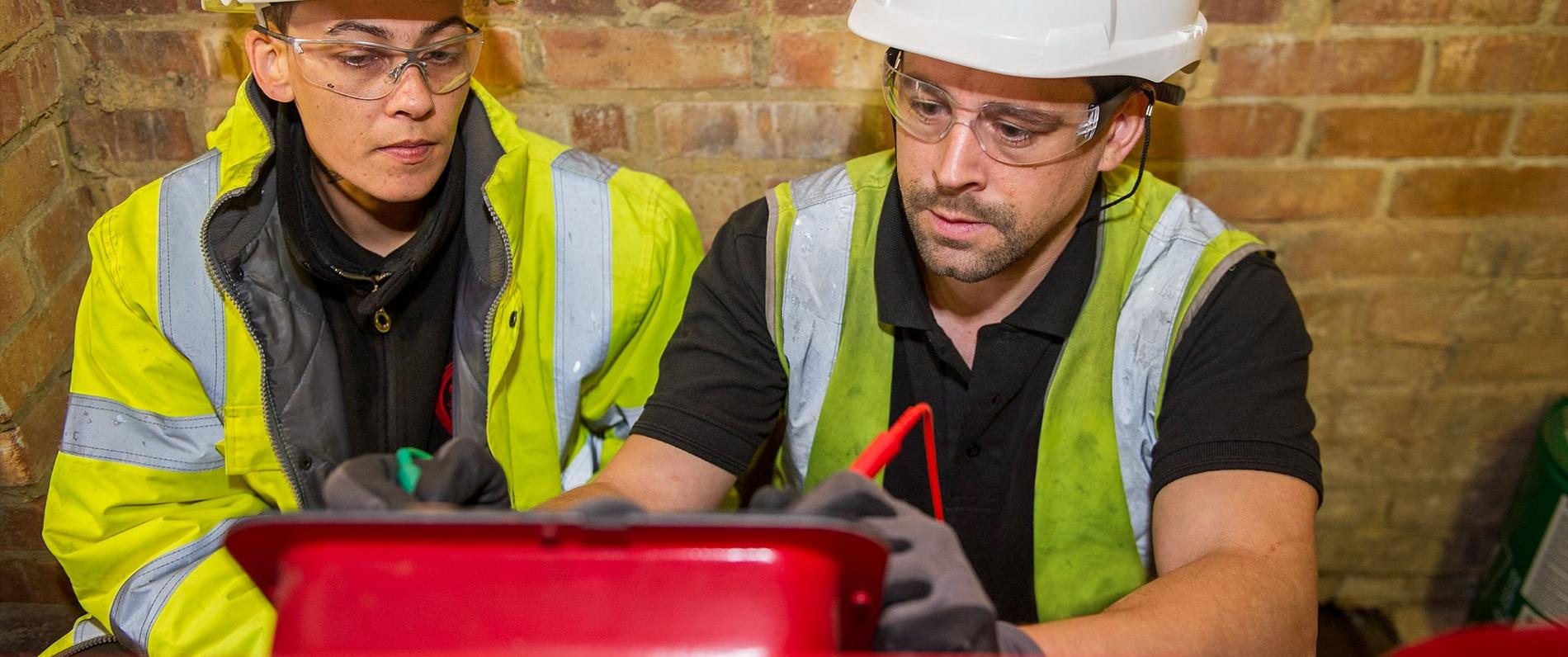 two electricians in gear working on a box