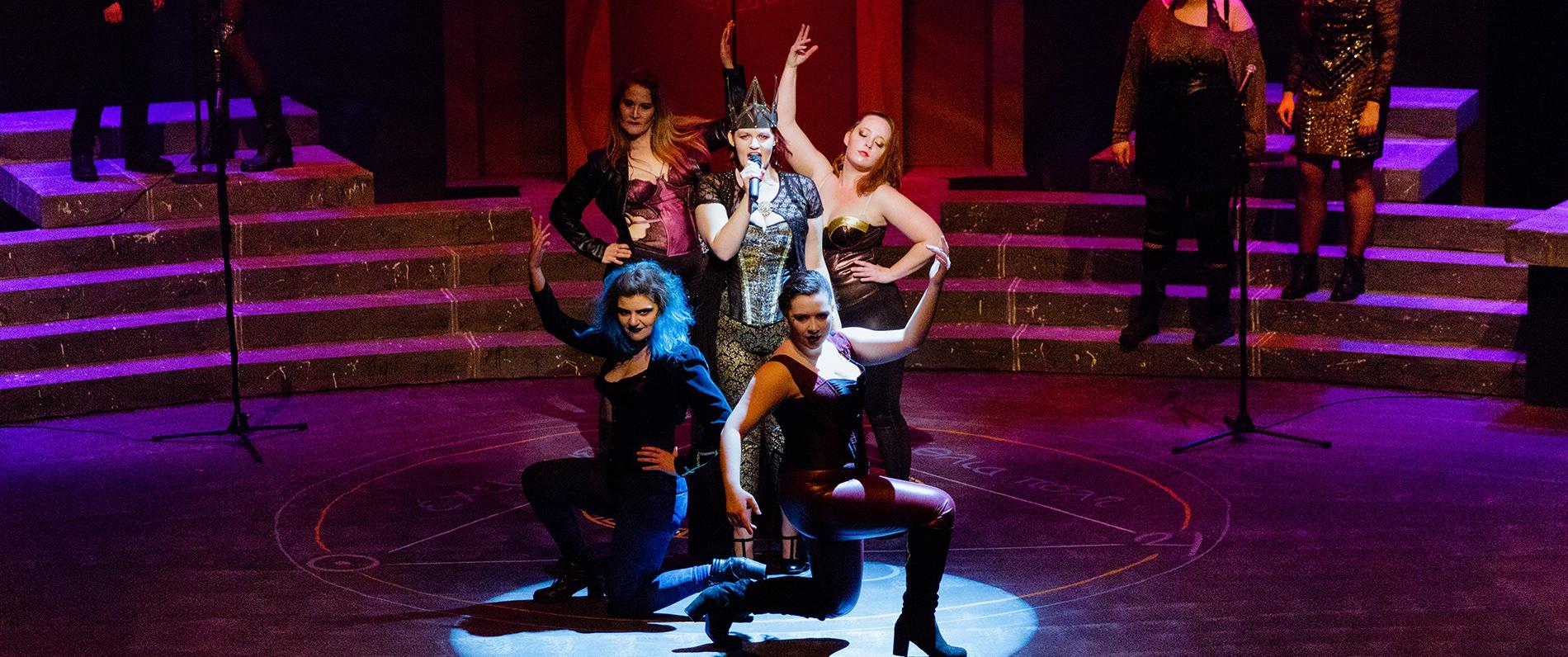 performers on stage pose while one speaks into a microphone