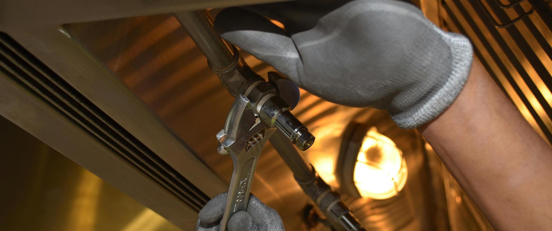a plumber's gloved hands carefully tightening a nut around a pipe