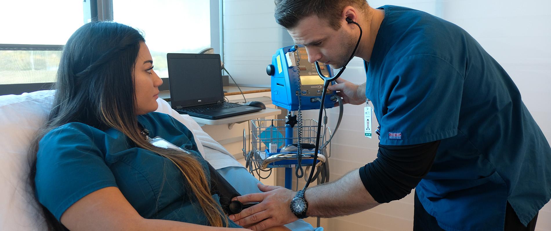 two bachelor of science in nursing students, one male and one female, practice taking blood pressure in the LCC nursing clinic