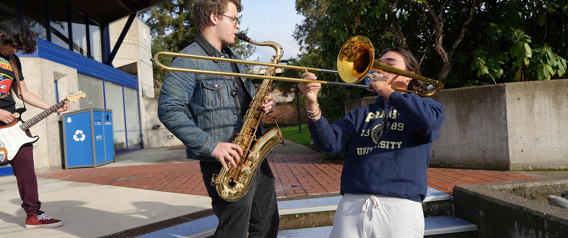 three music students play an electric guitar, a saxophone, and a trumpet outside the LCC music building