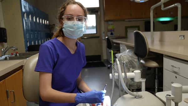 a dental hygiene student in scrubs and a mask working with dental cleaning tools