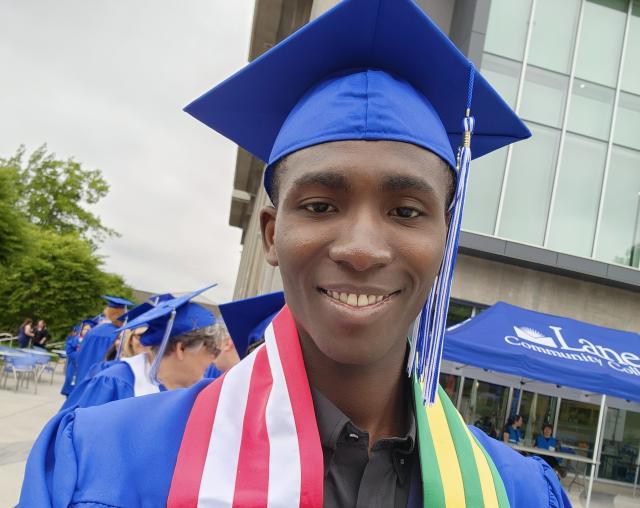 Kodjovi Amedjrovi wearing a graduation cap and gown with USA and Togo flags