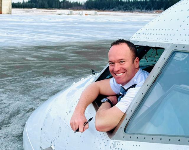 a pilot smiling and leaning out of window at the front of Boeing airplane on a snowy airfield