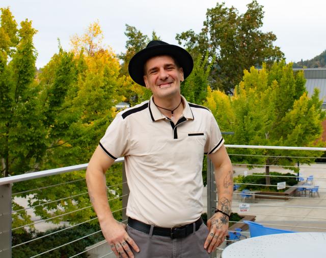 Wildland Fire Management student Cameron Stoker, a man in his 30s with a warm smile, tattoos, piercings, and stylish wide-brim hat posing by trees