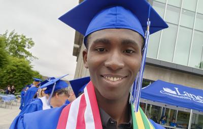 Kodjovi Amedjrovi wearing a graduation cap and gown with USA and Togo flags