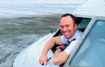 a pilot smiling and leaning out of window at the front of Boeing airplane on a snowy airfield