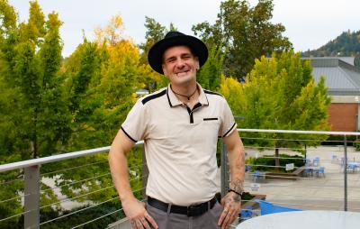 Wildland Fire Management student Cameron Stoker, a man in his 30s with a warm smile, tattoos, piercings, and stylish wide-brim hat posing by trees
