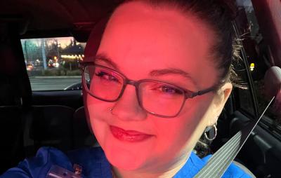 a young woman, a medical assistant student, in blue scrubs, red lipstick, and fashionable glasses taking a selfie