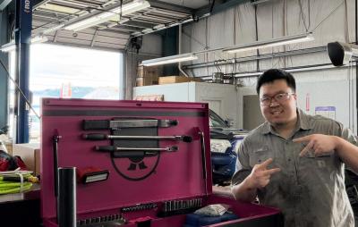 Leo Kim, an automotive and business student, wearing mechanics gear and smiling and posing in a garage 