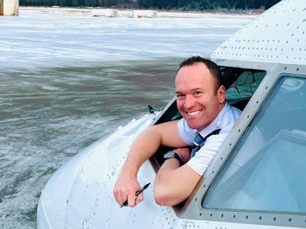 a pilot smiling and leaning out of window at the front of Boeing airplane on a snowy airfield