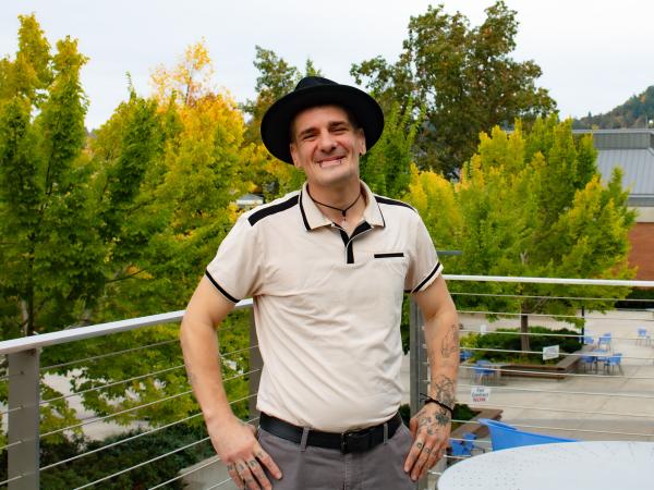 Wildland Fire Management student Cameron Stoker, a man in his 30s with a warm smile, tattoos, piercings, and stylish wide-brim hat posing by trees