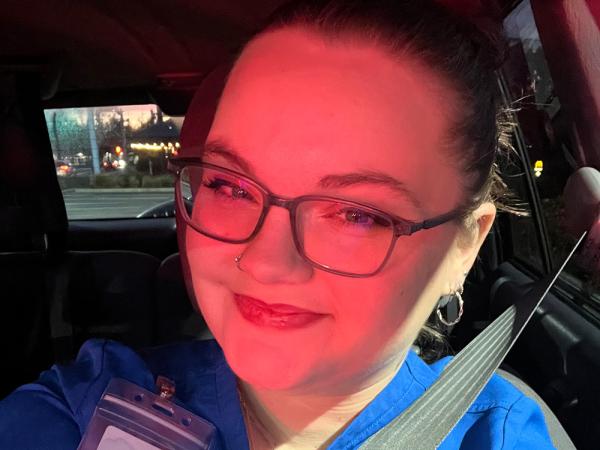 a young woman, a medical assistant student, in blue scrubs, red lipstick, and fashionable glasses taking a selfie