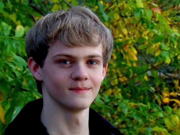 Nathan Matthews, an Early College and pre-med student, smiles with green foliage in background