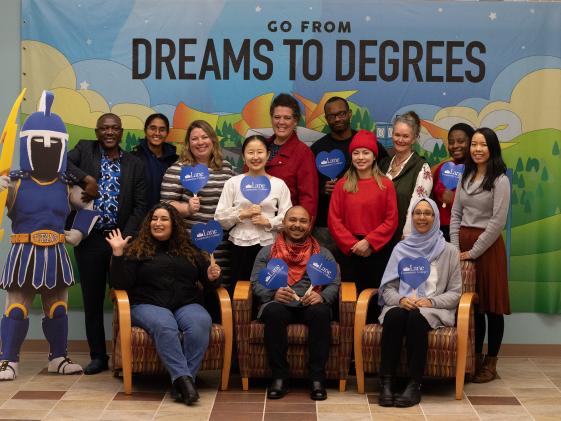 Program staff members smiling in front of a sign which says "From Dreams to Degrees"