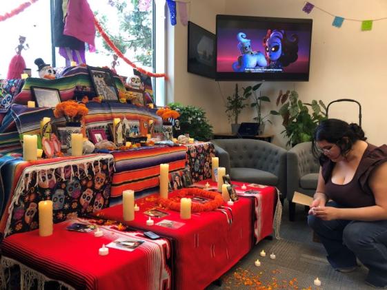 a young Latina woman sets up an ofreda with candle and marigolds in the Multicultural Center for Dia de los muertos