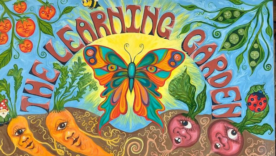 A colorful painted Learning Garden sign with a big butterfly and anthropomorphic carrots, radishes, and tomatoes