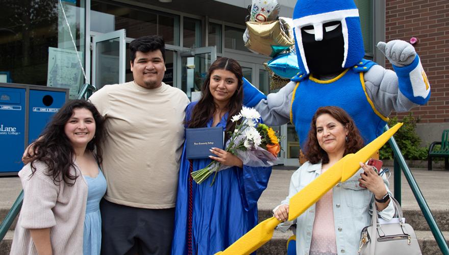 a graduating student poses with her family and Ty the Titan in front of Building 1