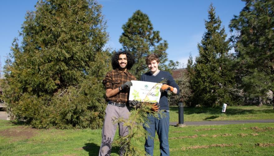 two "tree stewards," student workers who help plant trees, holding an arbor day foundation sign and smiling