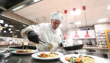 A culinary school student in chef uniform plating food in the kitchen