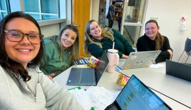 Four business bachelors students, women of various ages, take a selfie in together as they wait for class to start
