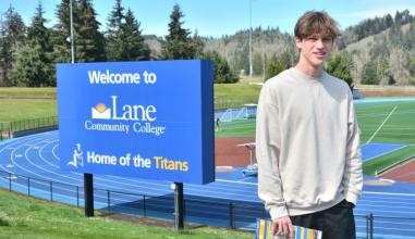 a high school student on a campus tour poses in front of our track with forest and hills in the background
