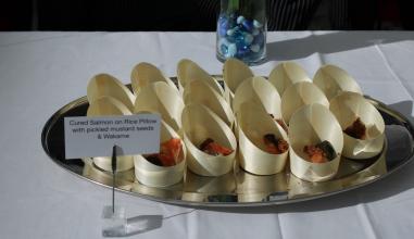 a plate of salmon sashmi on rice pillows with seaweed and pickled mustard seed in bamboo cups