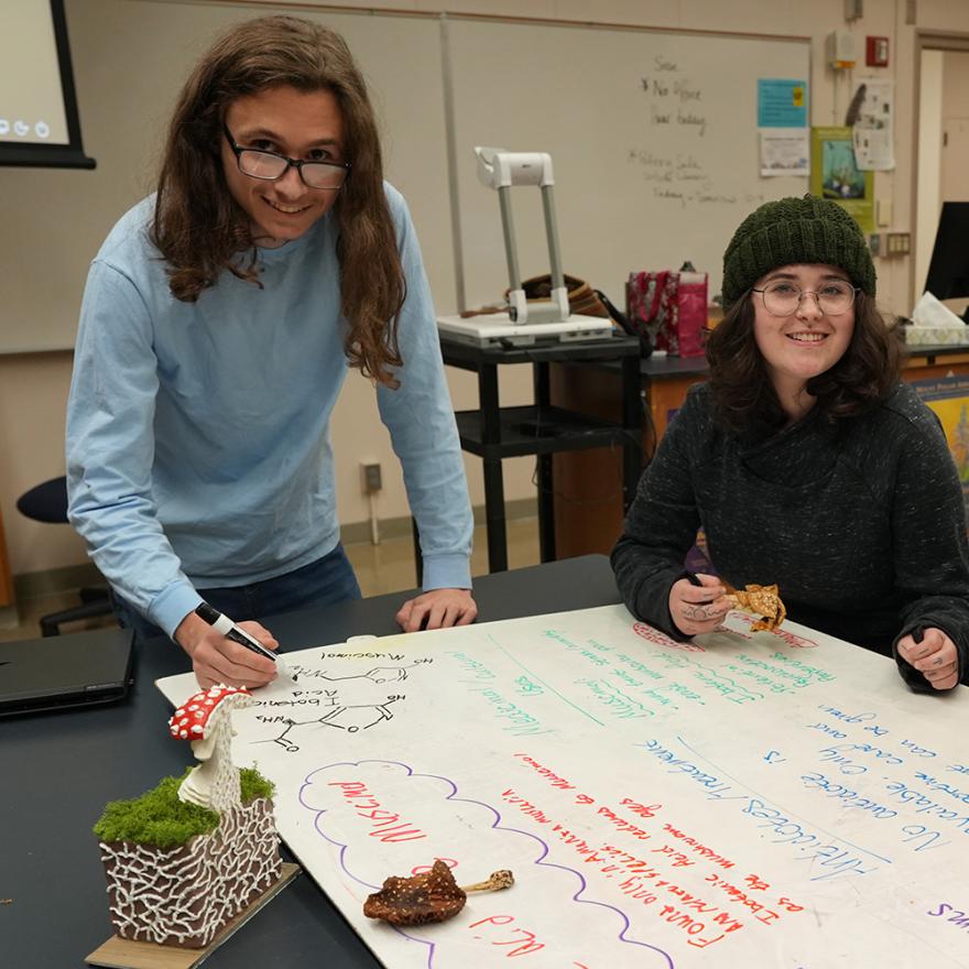 two students, a young man and woman, studying mushrooms with fun models in a biology class