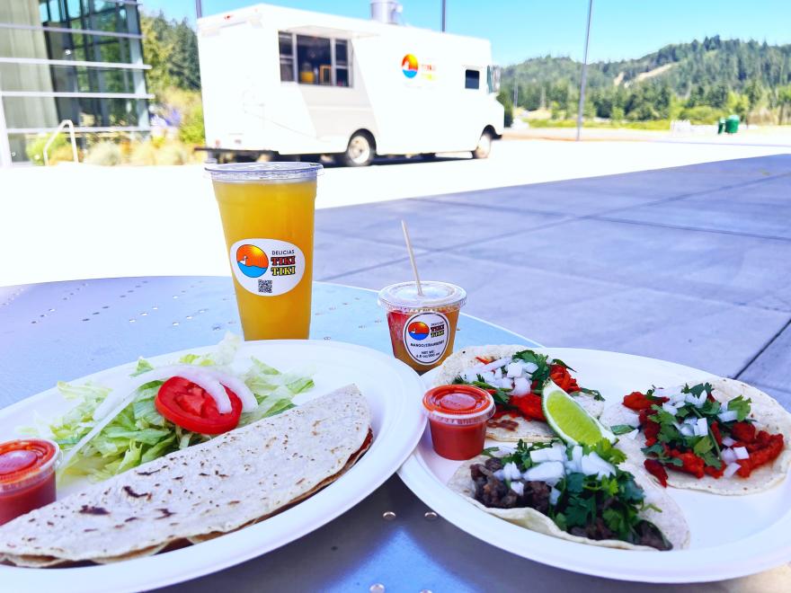 plates with tacos and fresh salsa with a tropical fruit drink and food truck in the background
