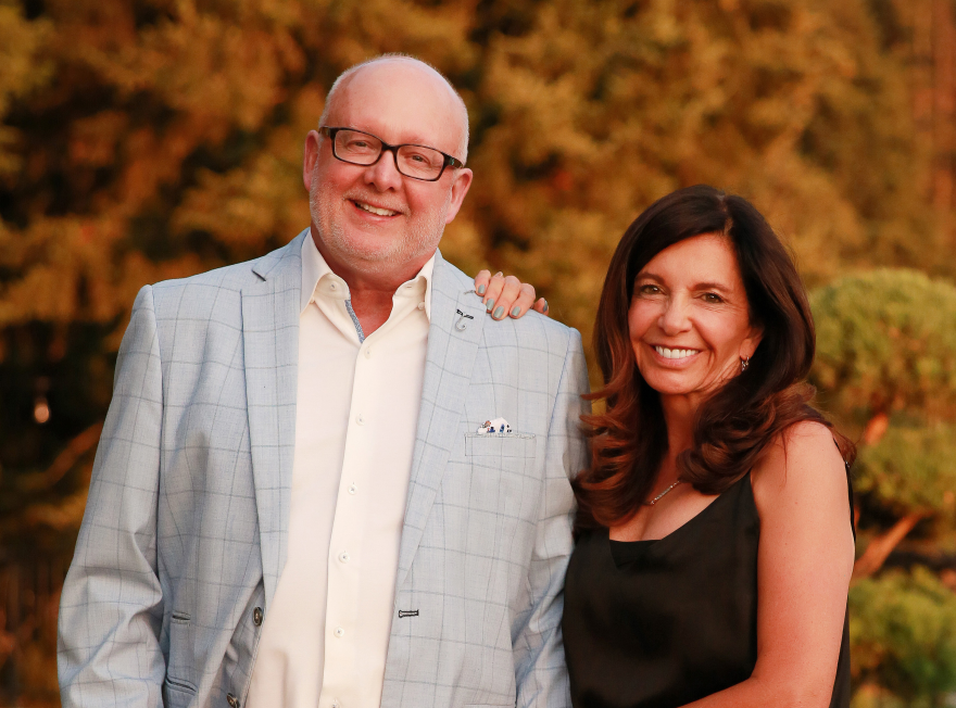 Man in blazer standing next to dark haired women with autumn trees in background