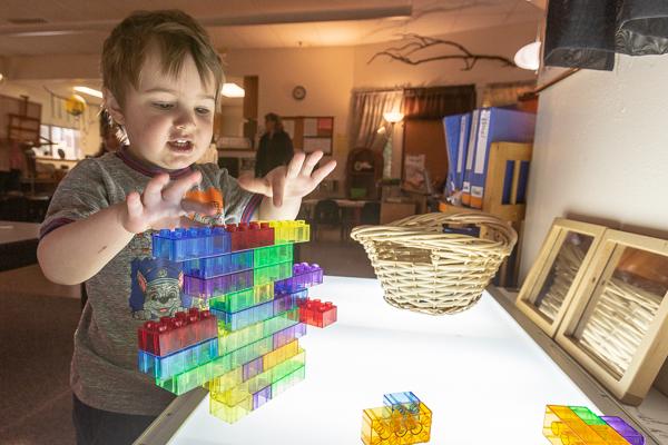 boy plays with translucent colored building blocks on a light table