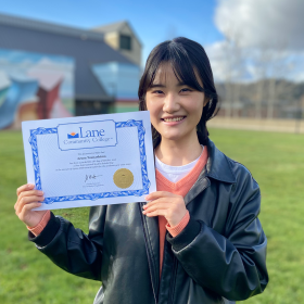 An international student, a young Japanese woman, smiles and shows off her LCC degree
