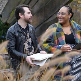 two students chat while holding notebooks and next to a fountain