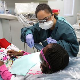 a friendly dental hygenist examines a little girl's teeth