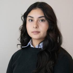a young woman with long, dark wavy hair, big brown eyes, and a nose piercing