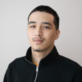 a young man with short dark hair and a goatee, wearing a black zip-up sweater