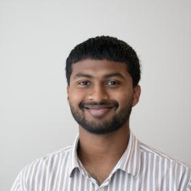 a young man with dark skin, brown eyes, a striped button up shirt, and a warm smile