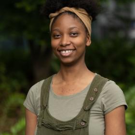 a young Black woman smiling and wearing green overalls and her curly hair in an cute updo