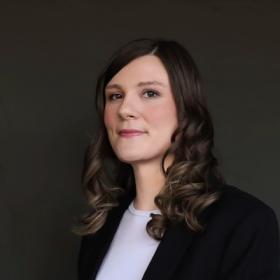 a young woman with pink lipstick and curly brown hair in a professional headshot