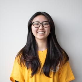 a young woman, with long dark hair and a bright yellow shirt, smiling