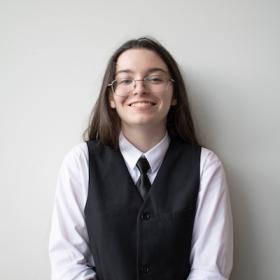a young woman with long dark hair and glasses, wearing a vest