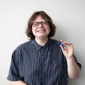 a young person, with long hair and glasses, laughing and playing with a fidget spinner